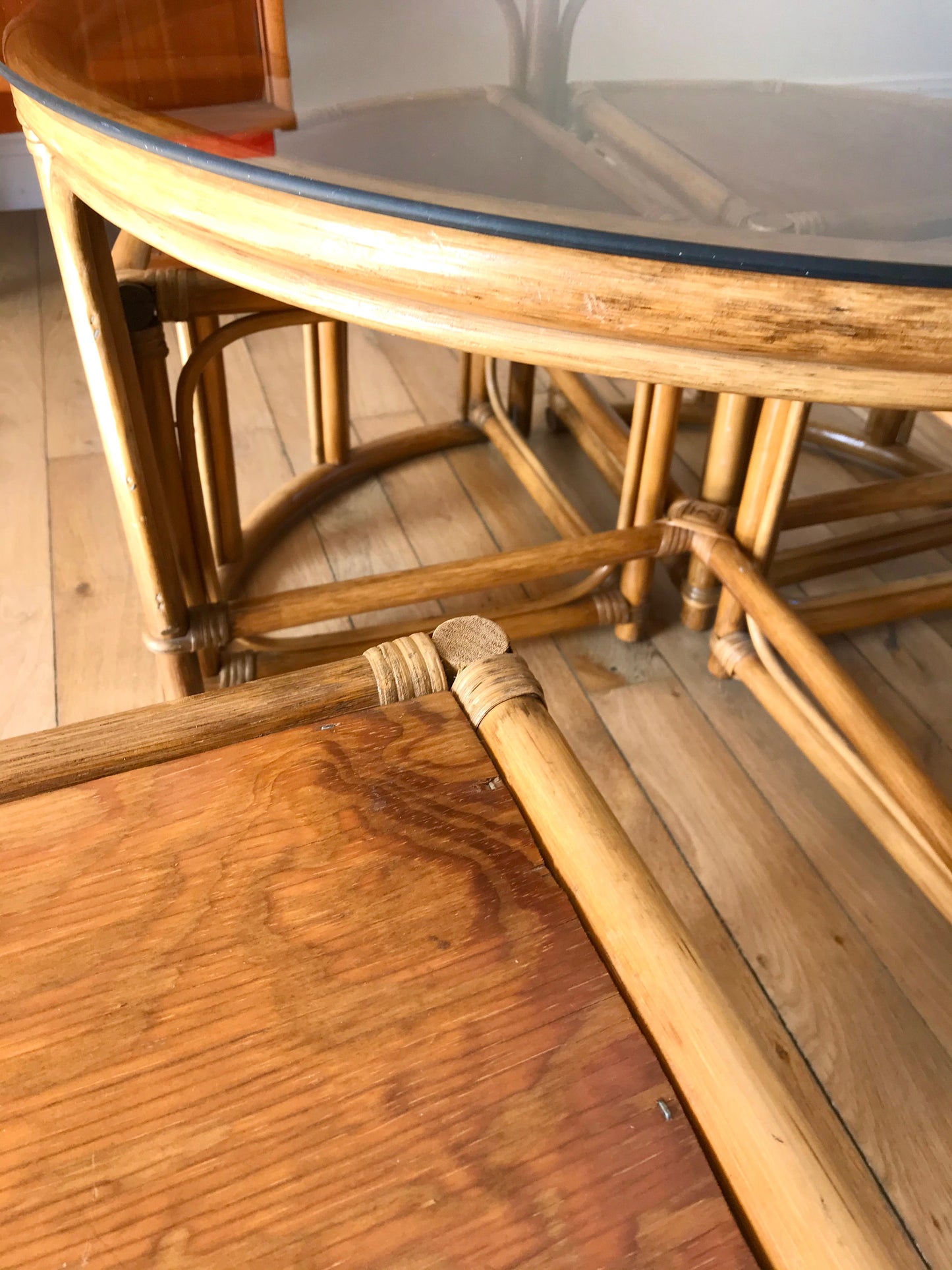 Ensemble en rotin design composé d'une table basse ronde avec plateau en verre fumé et 4 tabourets années 60