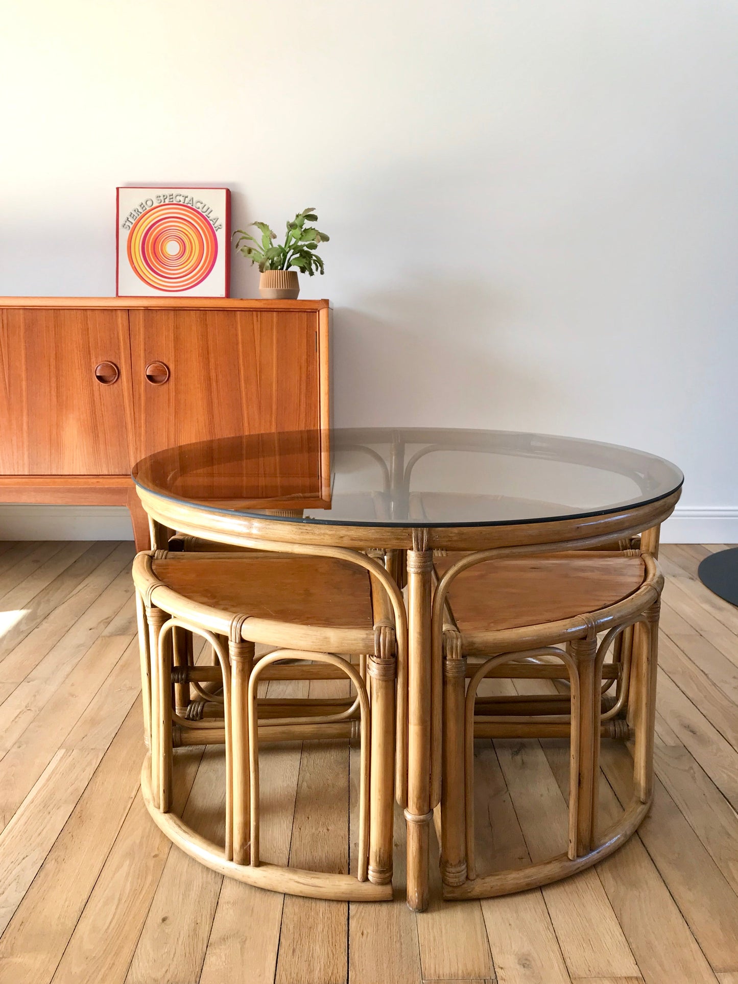 Ensemble en rotin design composé d'une table basse ronde avec plateau en verre fumé et 4 tabourets années 60